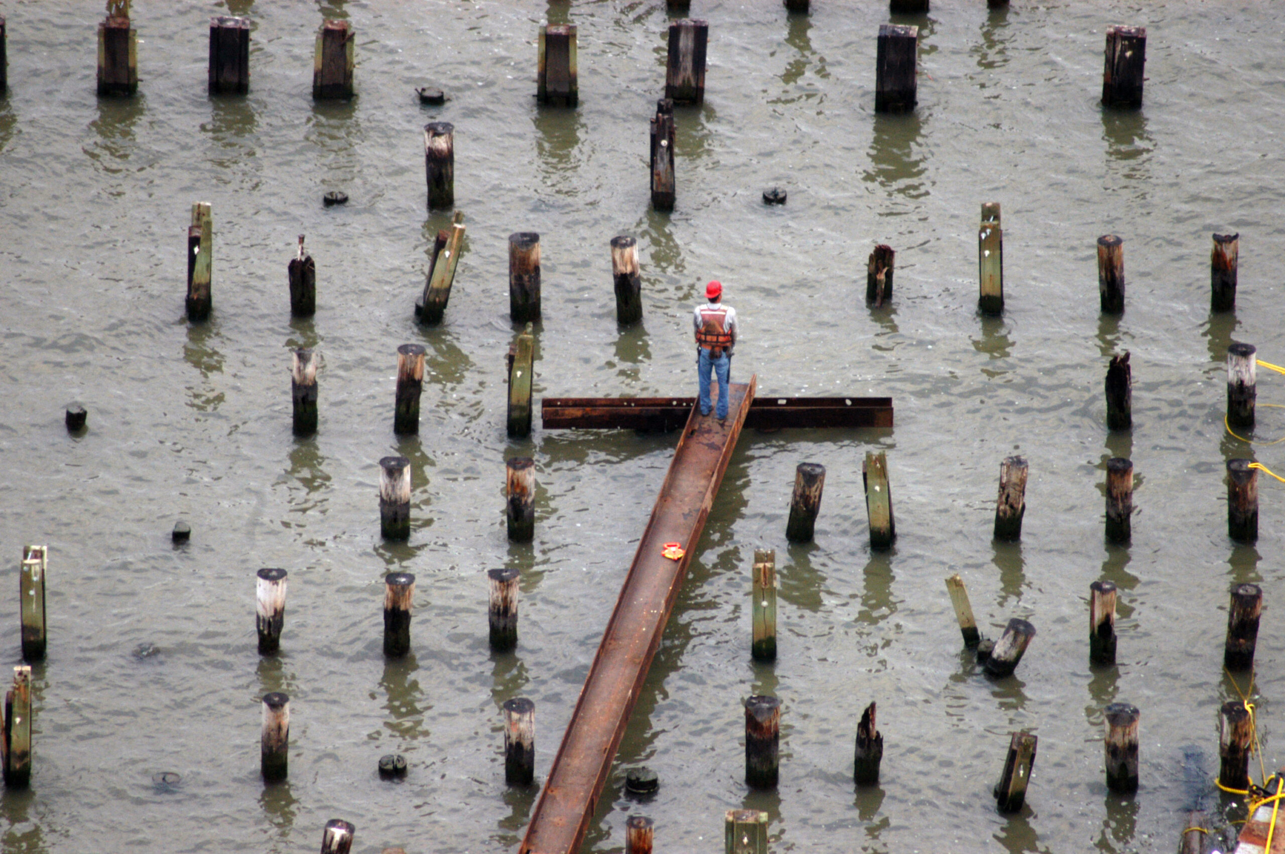 A construction worker standing on a beam in the middle of a pile field in the Hudson River.