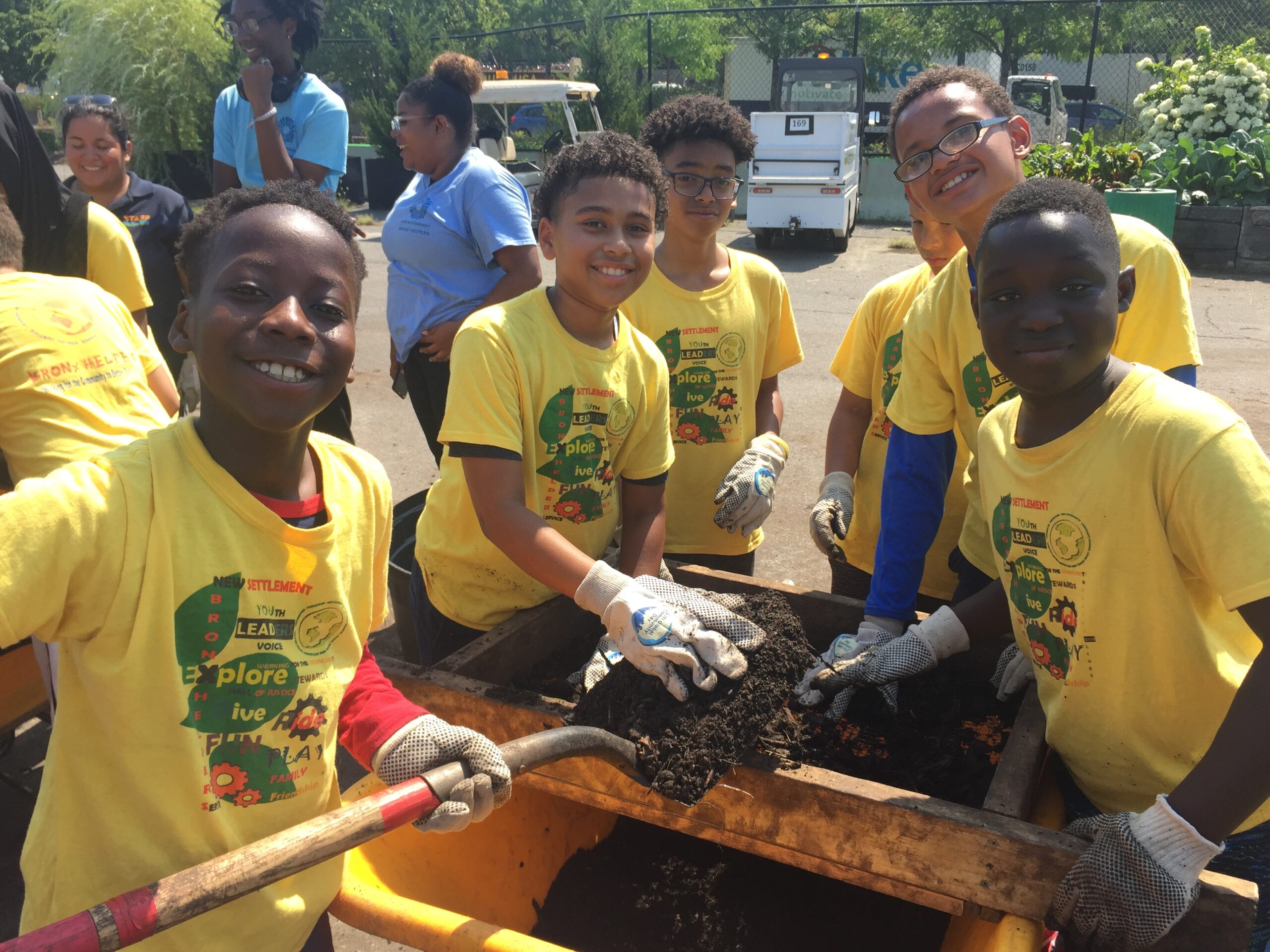 A group of six students volunteering with Hudson River Park's Community Compost program, shoveling compost into a wheelbarrow.