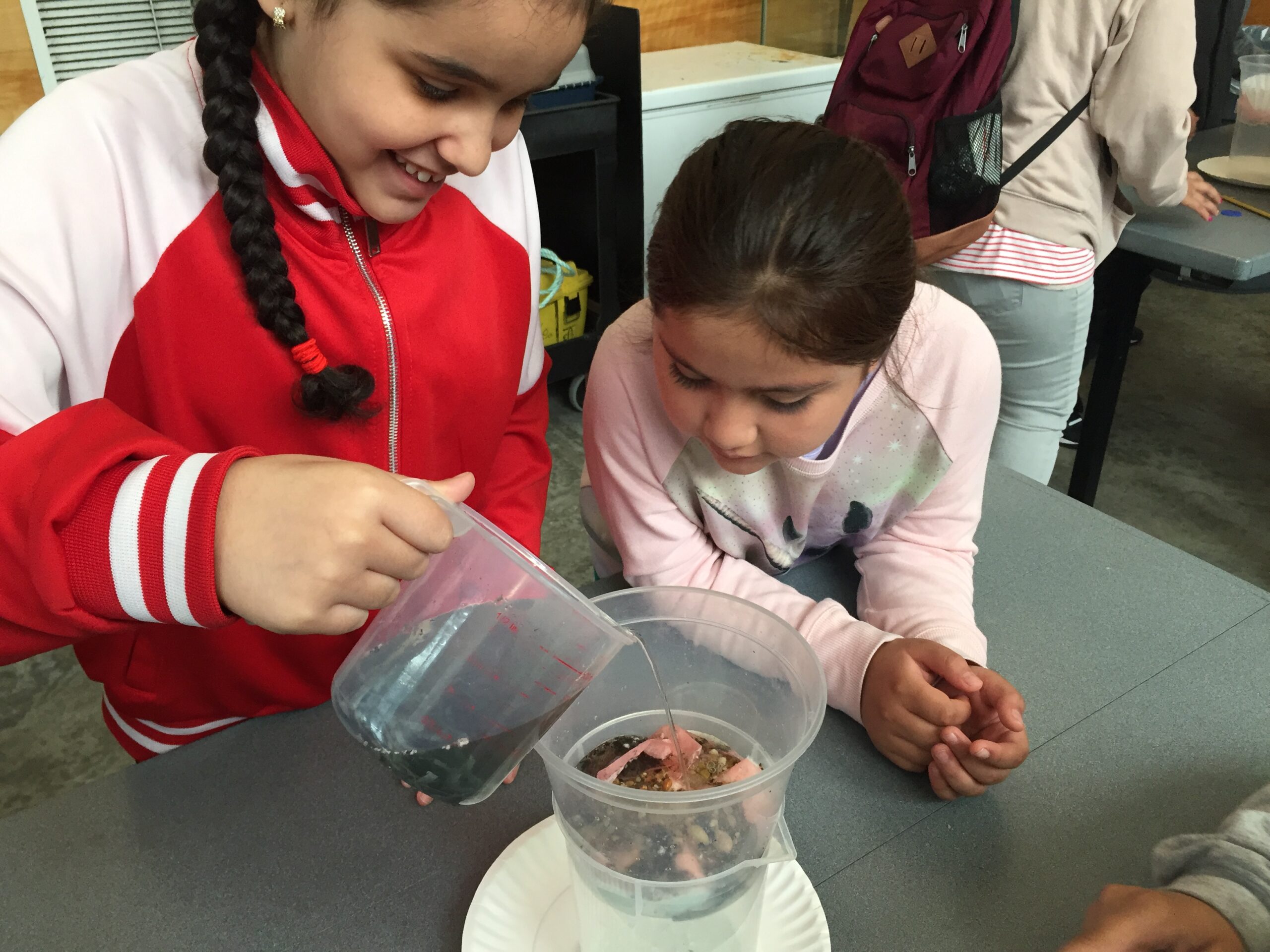 Two students pouring water into a container as part of a science classroom activity